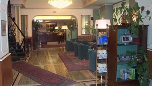 A hotel lobby with a grand chandelier, a reception desk, a staircase, and a seating area with a coffee table. - Hotel Milano (Trieste)