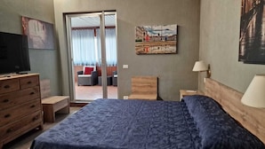 A hotel room with a bed, a wooden dresser, a television, a painting, and a view of the outside. - Hotel Milano (Trieste)