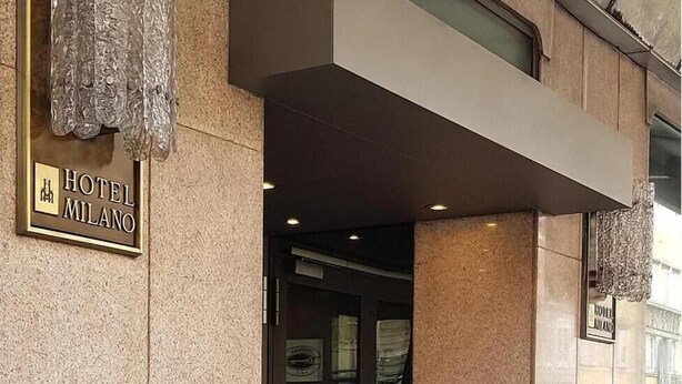 The exterior of Hotel Milano with a prominent entrance, a signboard, and decorative hanging elements. - Hotel Milano (Trieste)