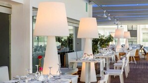 Ein Restaurant mit weißen Tischen und Stühlen, großen Lampen und einer Holzterrasse.