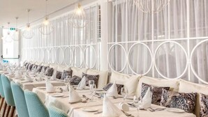 Ein Restaurant mit Tischen und Stühlen, weißen Tischdecken und gemusterten Kissen.