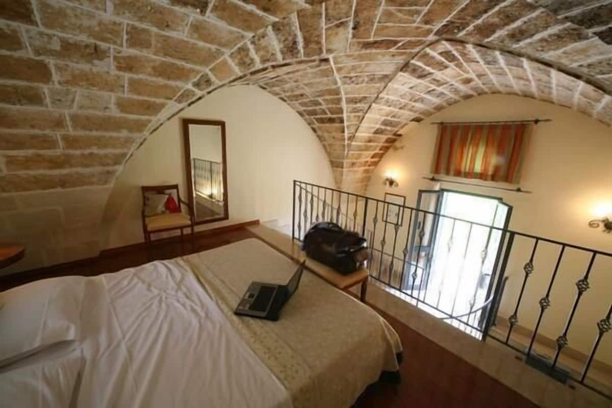 A bedroom with a bed, a laptop, a suitcase, and a view of a balcony with a railing.