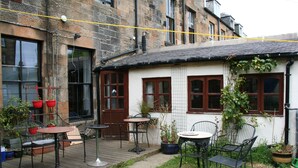 Une cour avec des espaces de repos en plein air, des plantes en pot et un bâtiment doté d’une façade carrelée et d’une porte en bois.