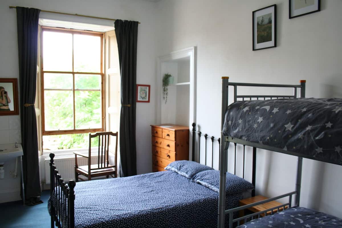 A bedroom with a bunk bed, a wooden dresser, a chair, and a window with curtains.