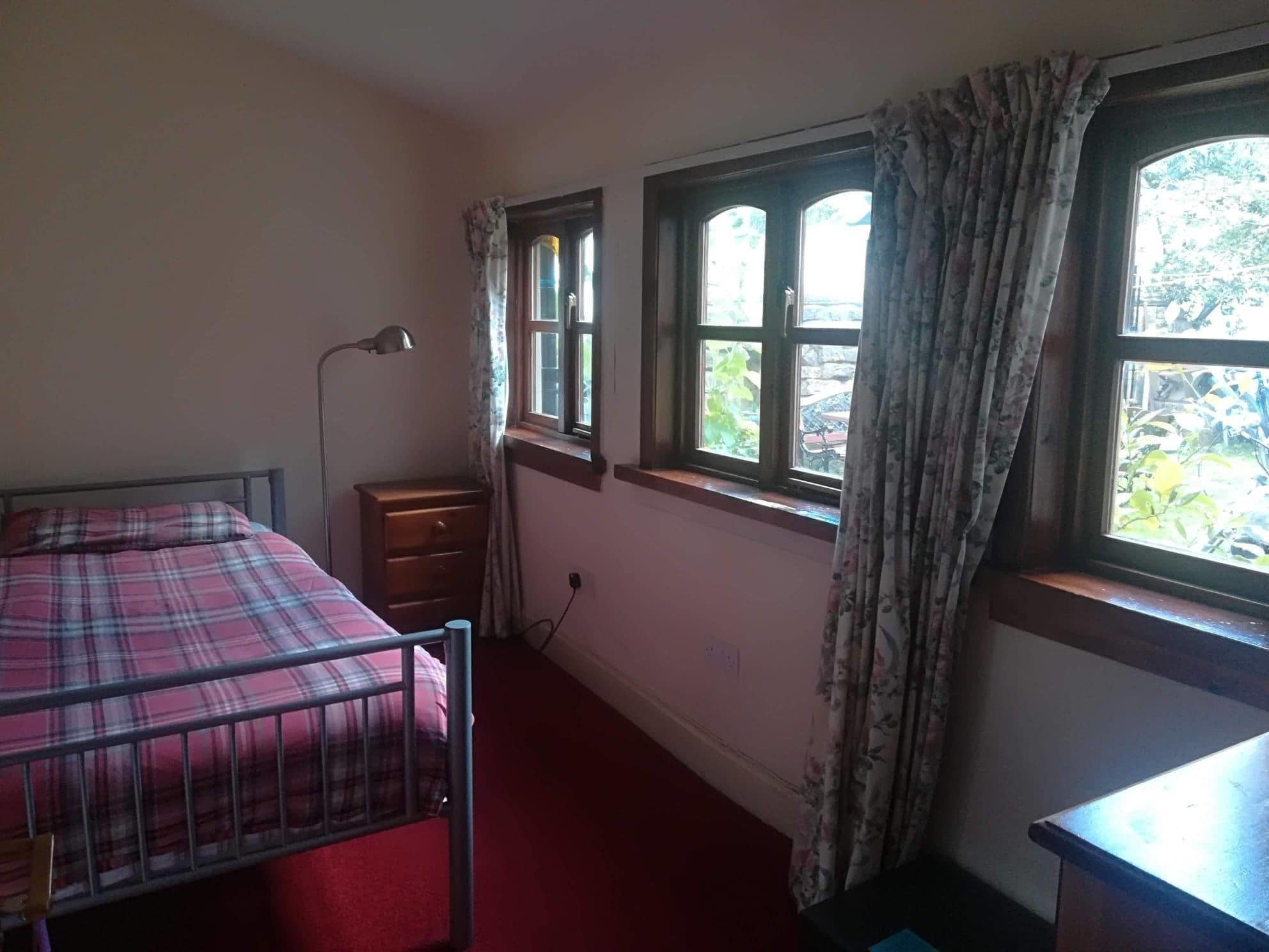 A bedroom with a bed, a dresser, a desk, and two windows with curtains.