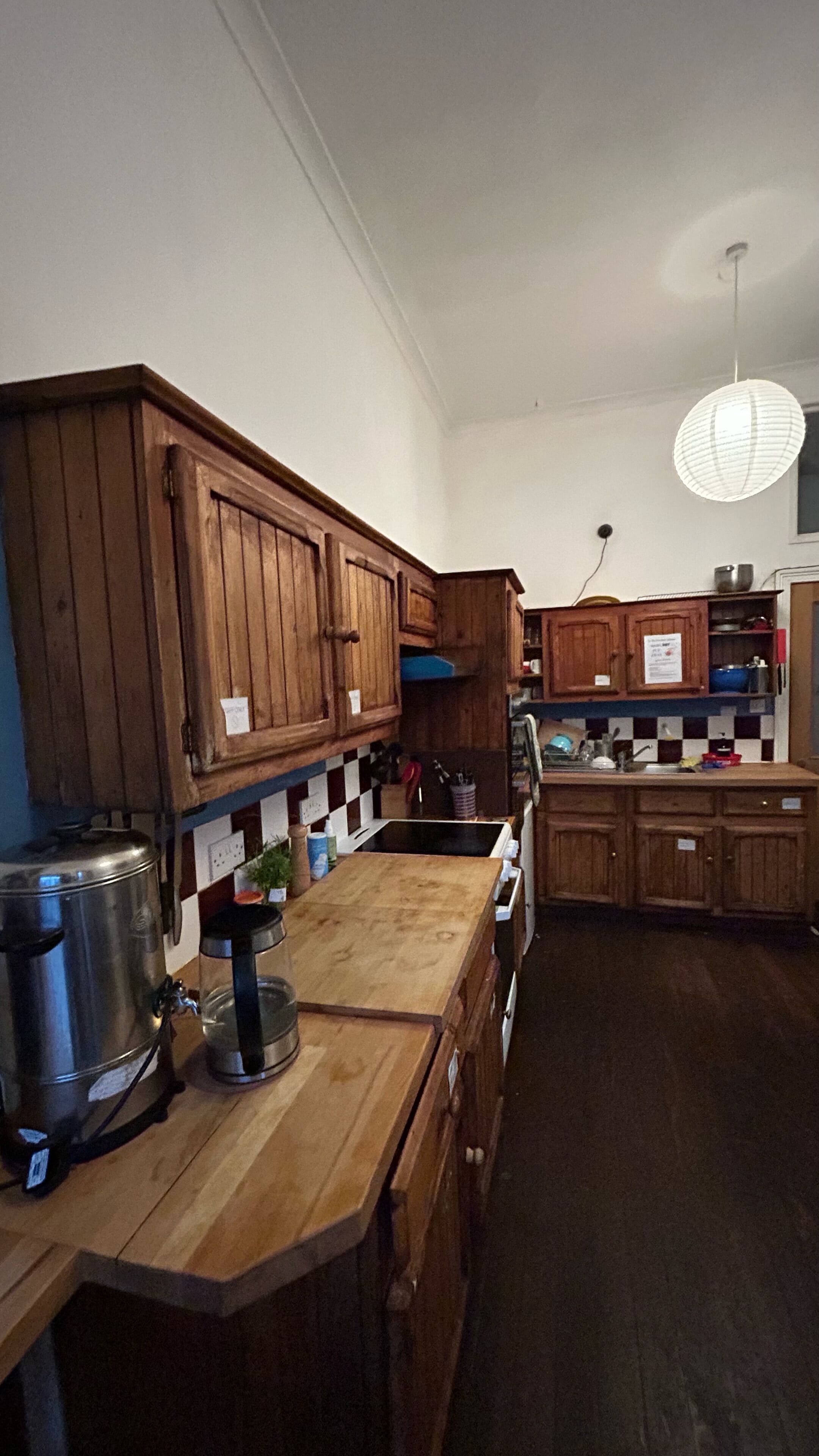 A kitchen with wooden cabinets, a stainless steel kettle, and a checkered backsplash.