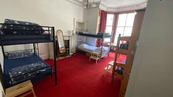 Une chambre avec des lits superposés, une petite table, un miroir et une fenêtre avec des rideaux.