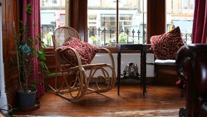 Une pièce chaleureuse avec un fauteuil à bascule en osier, une table et une vue sur la rue grâce à de grandes fenêtres.