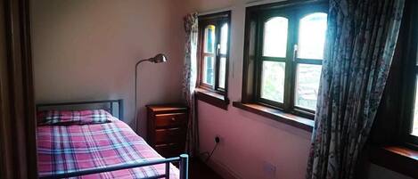 Un dormitorio con una cama individual, una lámpara de noche, una mesita de noche y una ventana con cortinas.