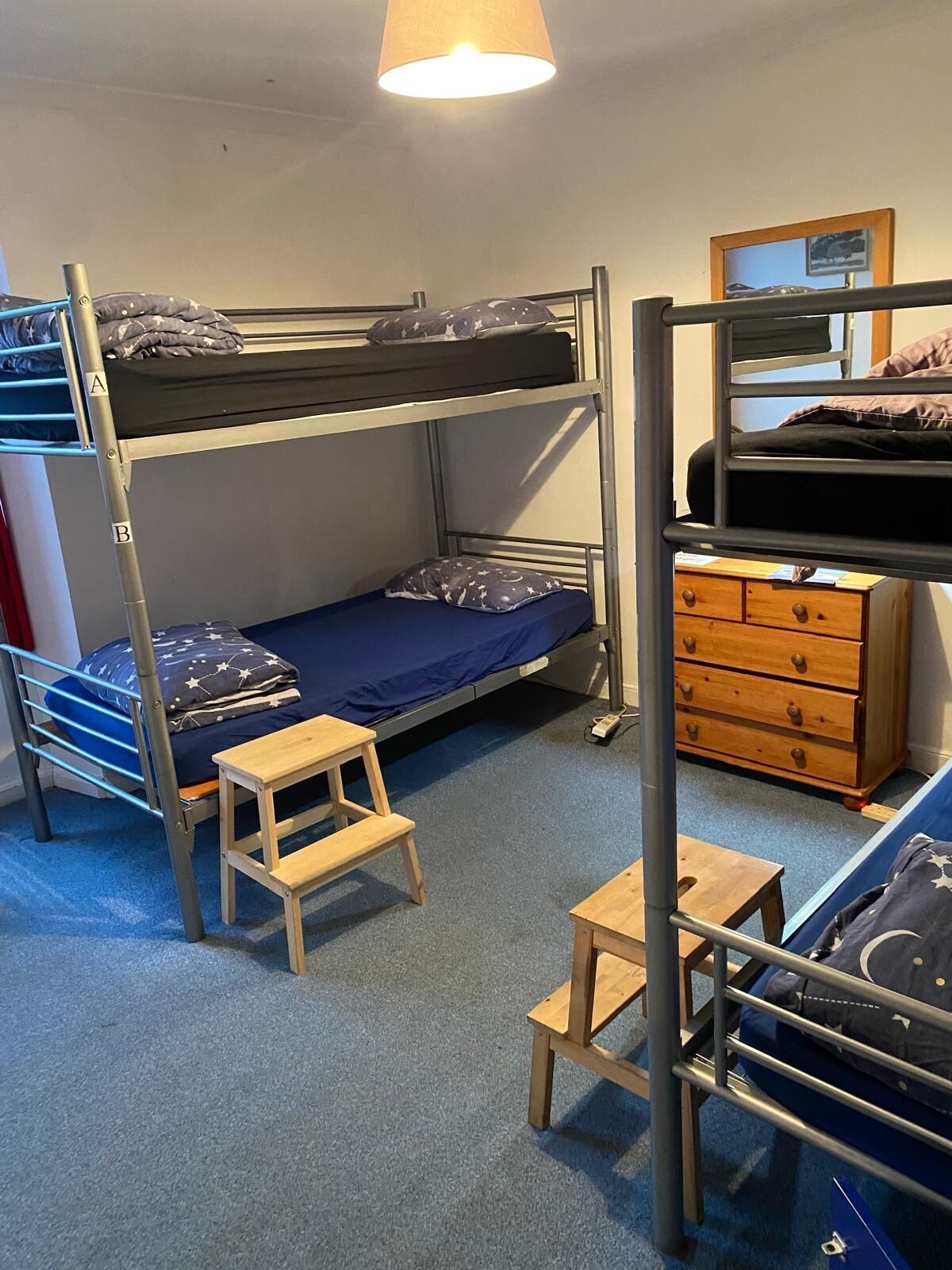 A bunk bed room with a desk, dresser, and a lamp.
