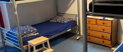 A bunk bed room with a desk, dresser, and a lamp.
