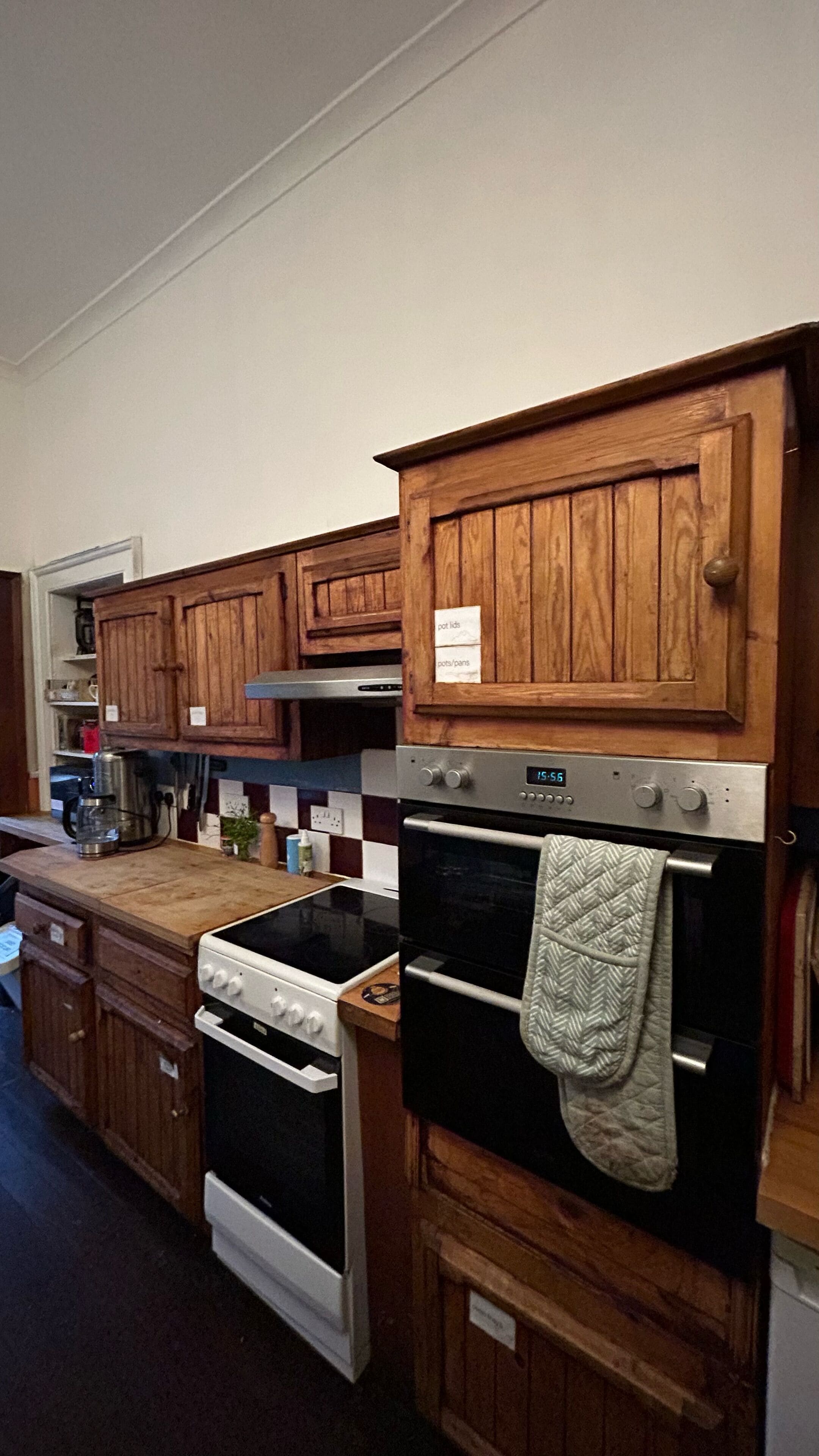 Una cuina amb armaris de fusta, una placa de cocció, un forn i una cafetera.