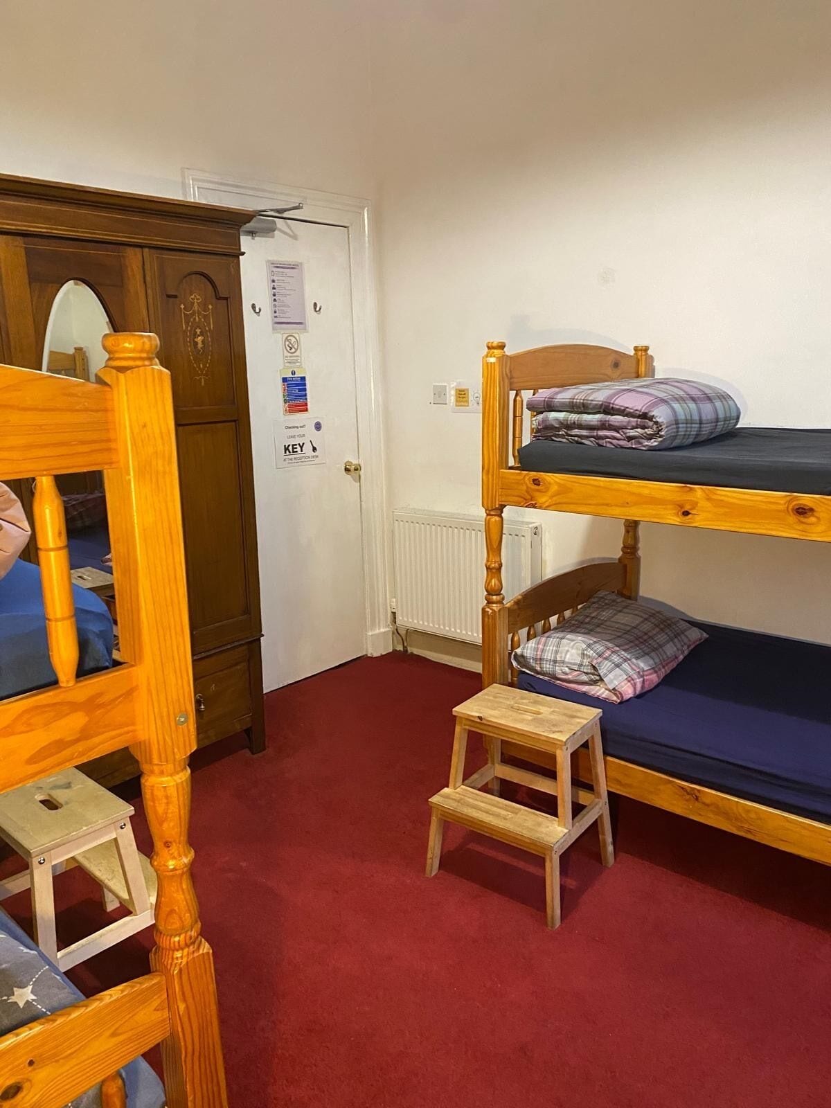 Un letto a castello con un piccolo sgabello di legno, una sedia di legno e una porta dotata di lettore per badge.