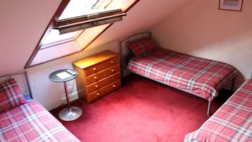 Une petite chambre mansardée de forme triangulaire, avec deux lits, une commode et une petite table.