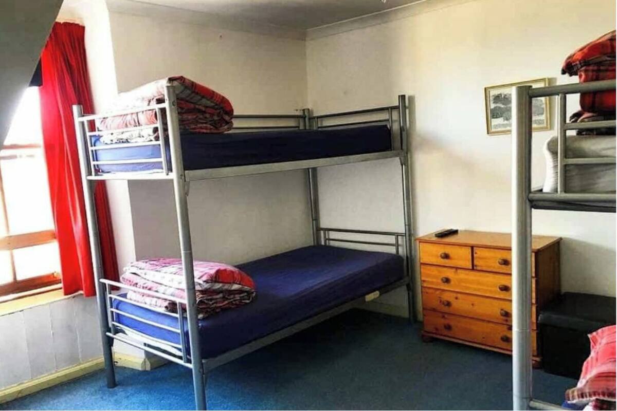 A bunk bed room with a dresser and a window with red curtains.