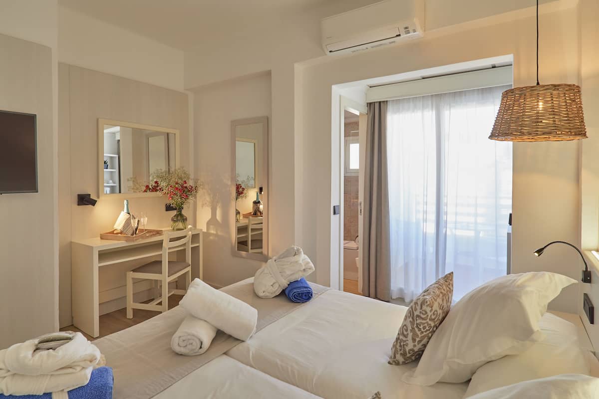 A hotel room with two beds, a desk, a mirror, and a window with curtains.