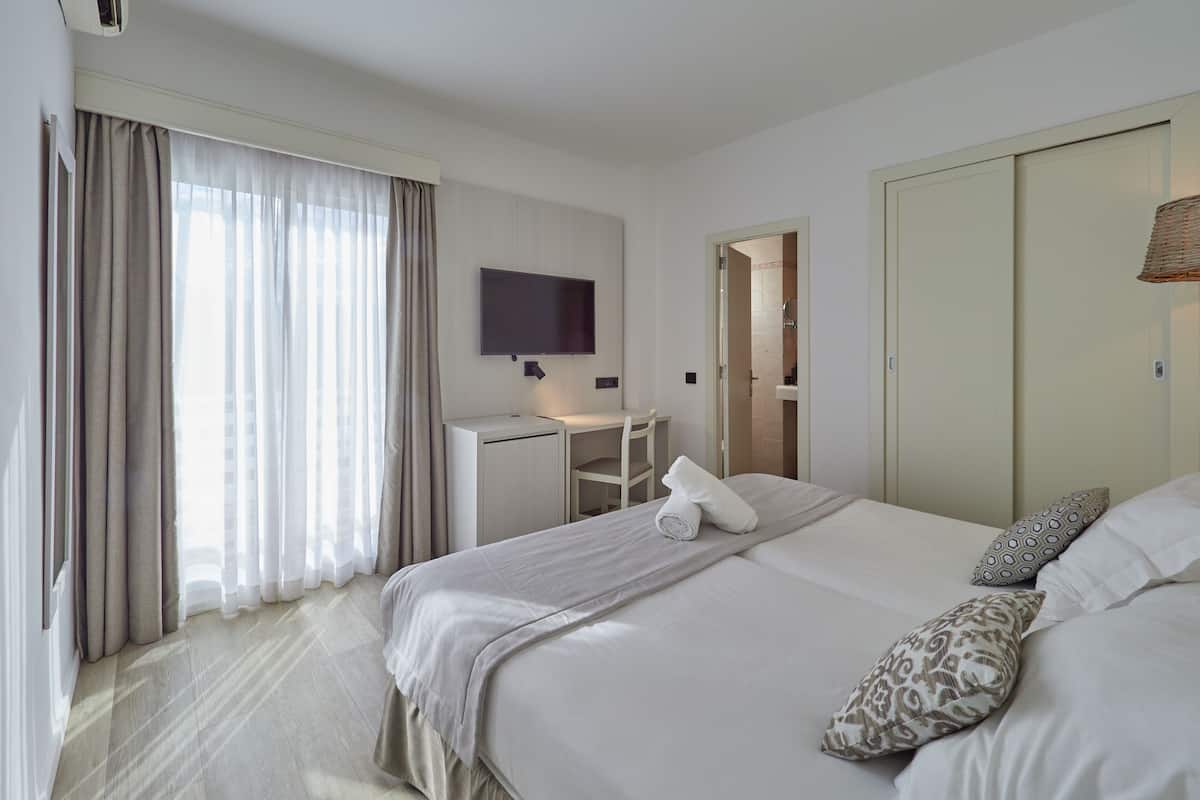 A hotel room with a bed, a desk, a TV, and a bathroom visible through an open door.