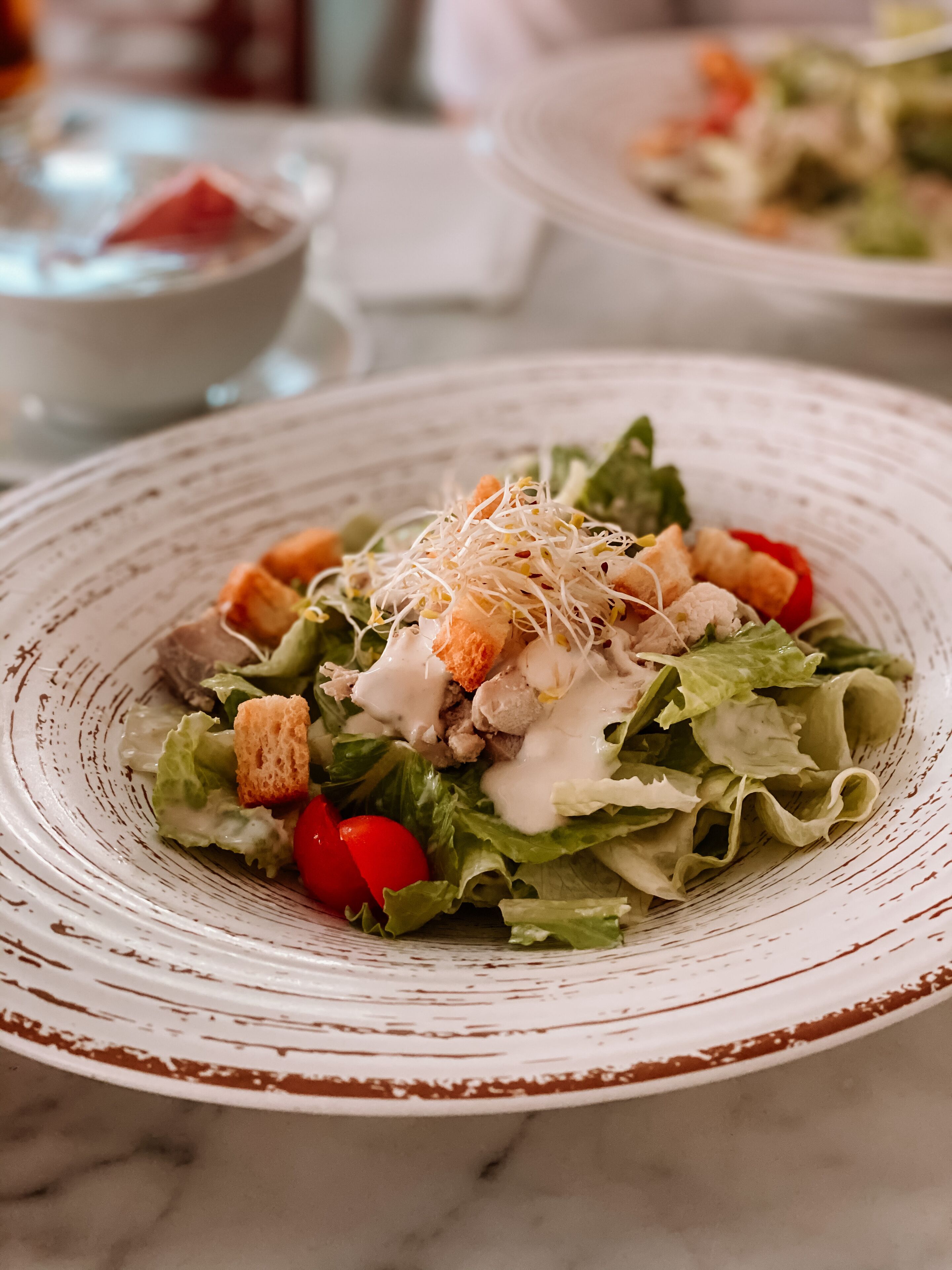 A plate of Caesar salad with croutons, shredded cheese, and cherry tomatoes.