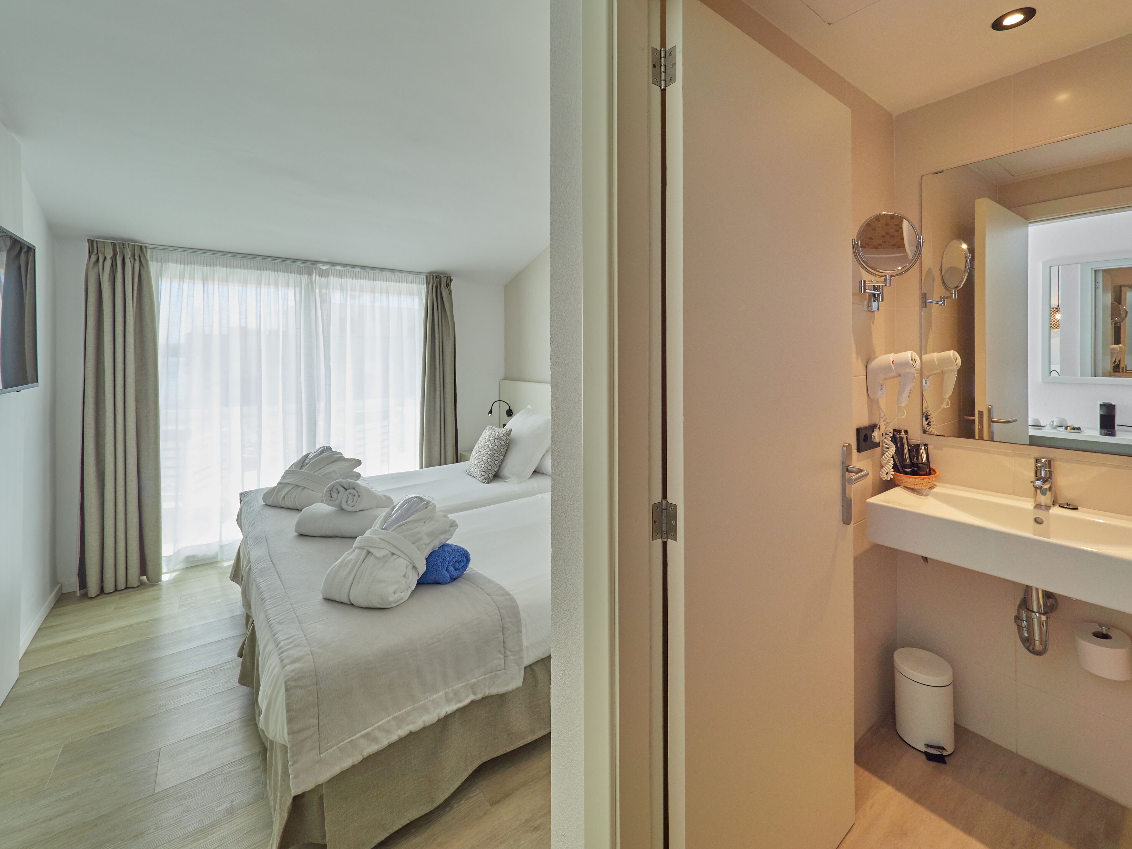 A hotel room with a bed, a bathroom with a sink and mirror, and a window with curtains.