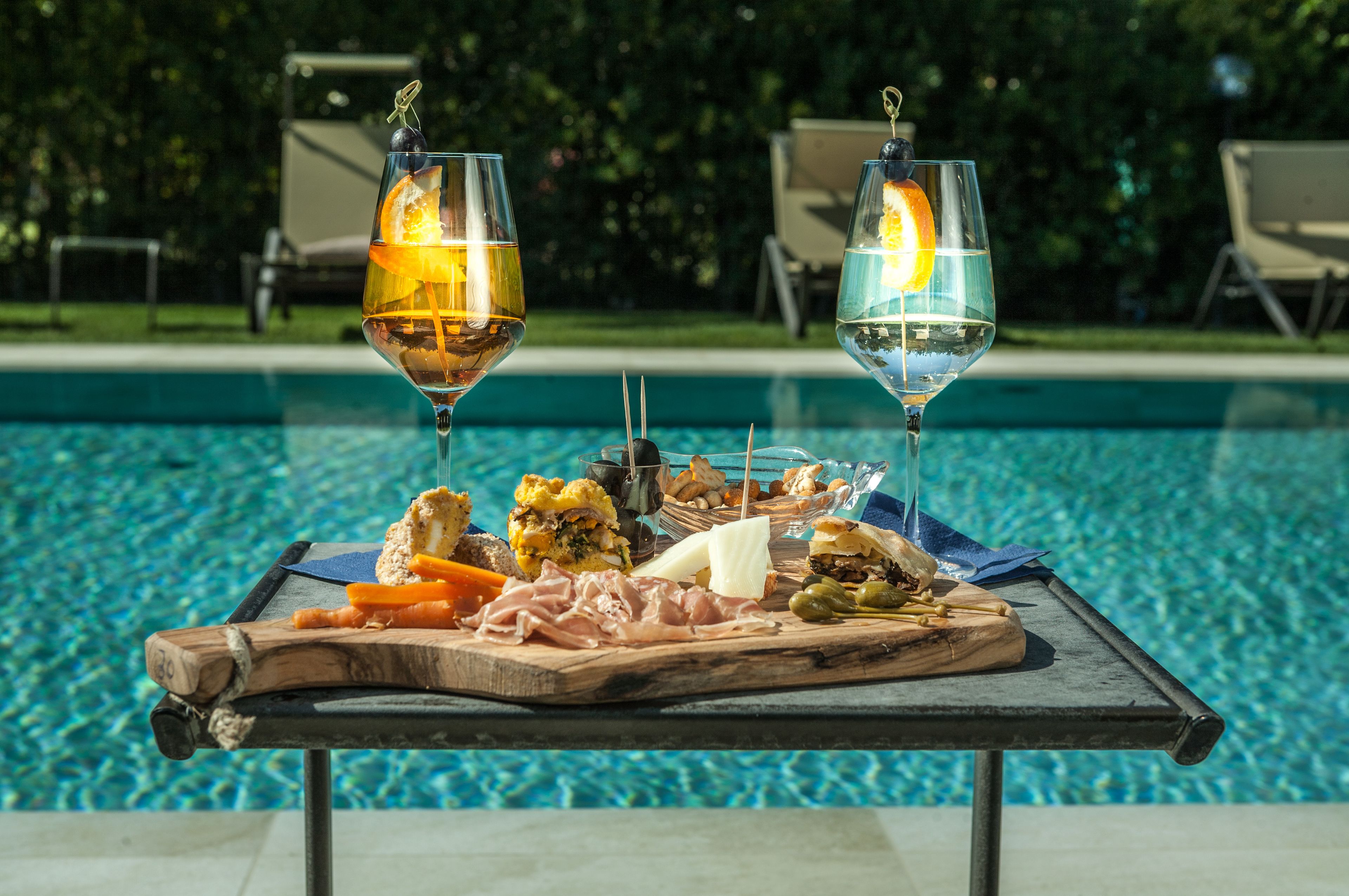 A poolside table with a charcuterie board and two glasses of wine.
