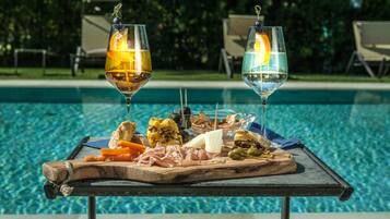 Una mesa junto a la piscina con una tabla de embutidos y dos copas de vino.