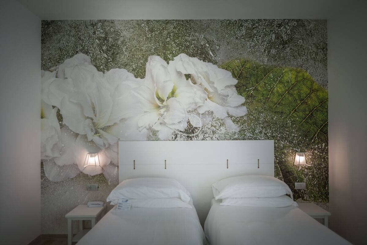 Un dormitorio con un gran mural floral en la pared, dos camas con ropa de cama blanca y lámparas de noche.