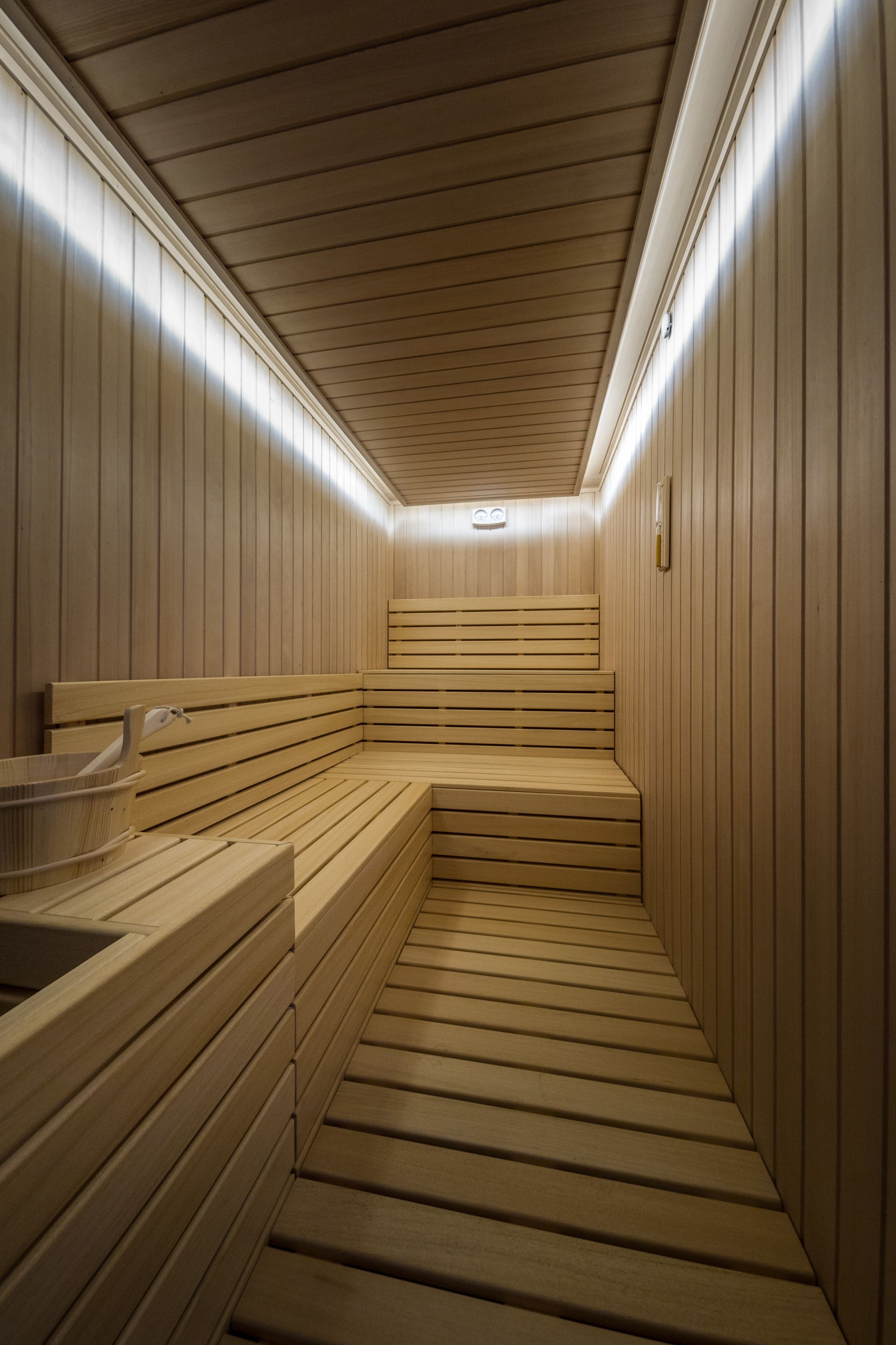 Una sauna con bancos de madera y un asiento de banco, paredes de madera y un techo con un accesorio de iluminación.