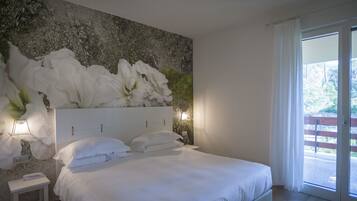 A bedroom with a large bed, a nightstand, a wall-mounted light, and a view of the outdoors through a sliding glass door.