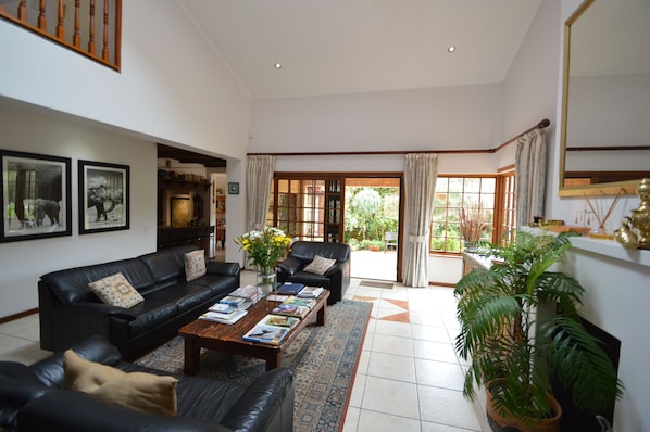 A spacious living room with a black leather sofa set, a coffee table with books, and a large window with curtains.