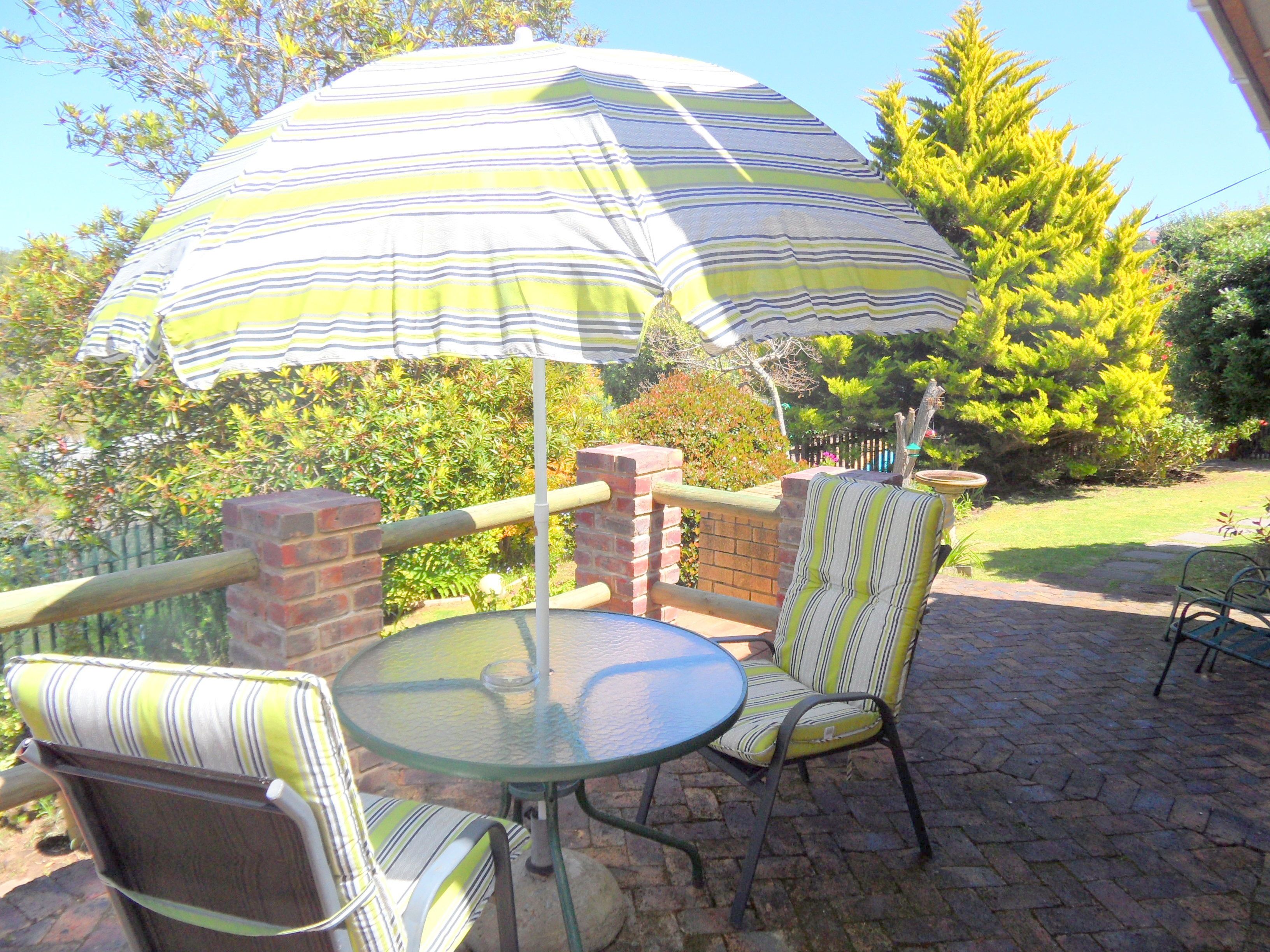 Une terrasse extérieure avec une table ronde en verre, des chaises à rayures et un parasol à rayures offrant de l’ombre.
