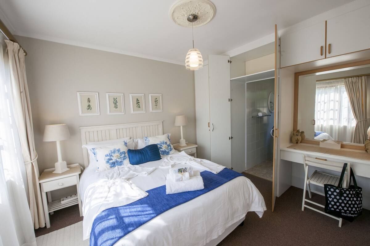 A hotel room with a bed, nightstands, a desk, a mirror, and a wardrobe.