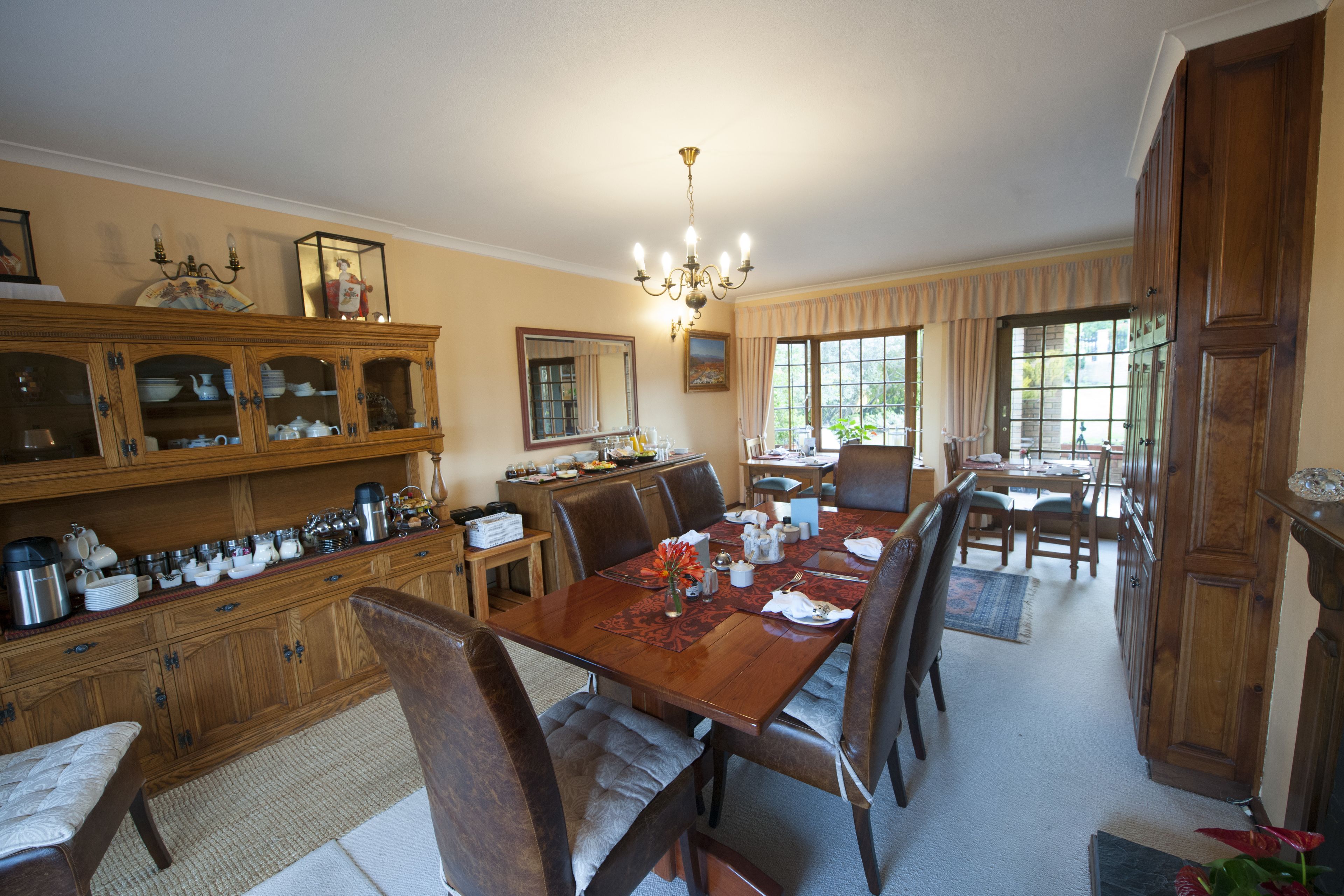 Un coin repas avec une table en bois dressée pour quatre personnes, entourée de chaises. On aperçoit également une cuisine avec des placards en bois et une table à manger à l’arrière-plan.