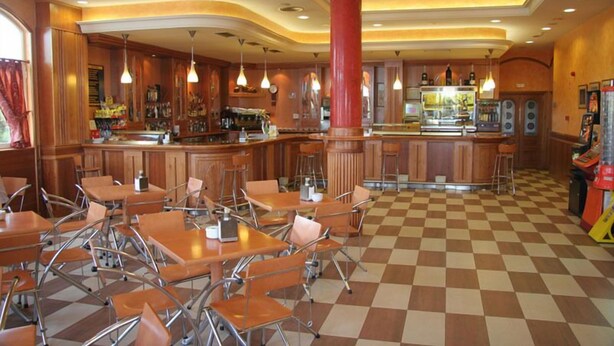 A restaurant with checkered flooring, wooden booths, and a central bar area. - Hotel Camino Real (Valdefresno)