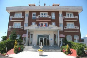 A multi-story hotel with a central entrance, balconies, and a fountain in the front.
