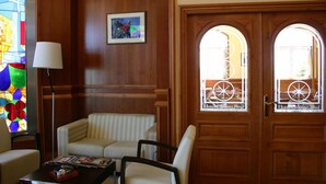A hotel lobby with a wooden paneled wall, a stained glass window, a sofa, a chair, and a door with a circular window. - Hotel Camino Real (Valdefresno)