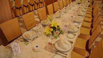 Una larga mesa de banquete dispuesta con manteles blancos, platos con detalles dorados y cristalería transparente.