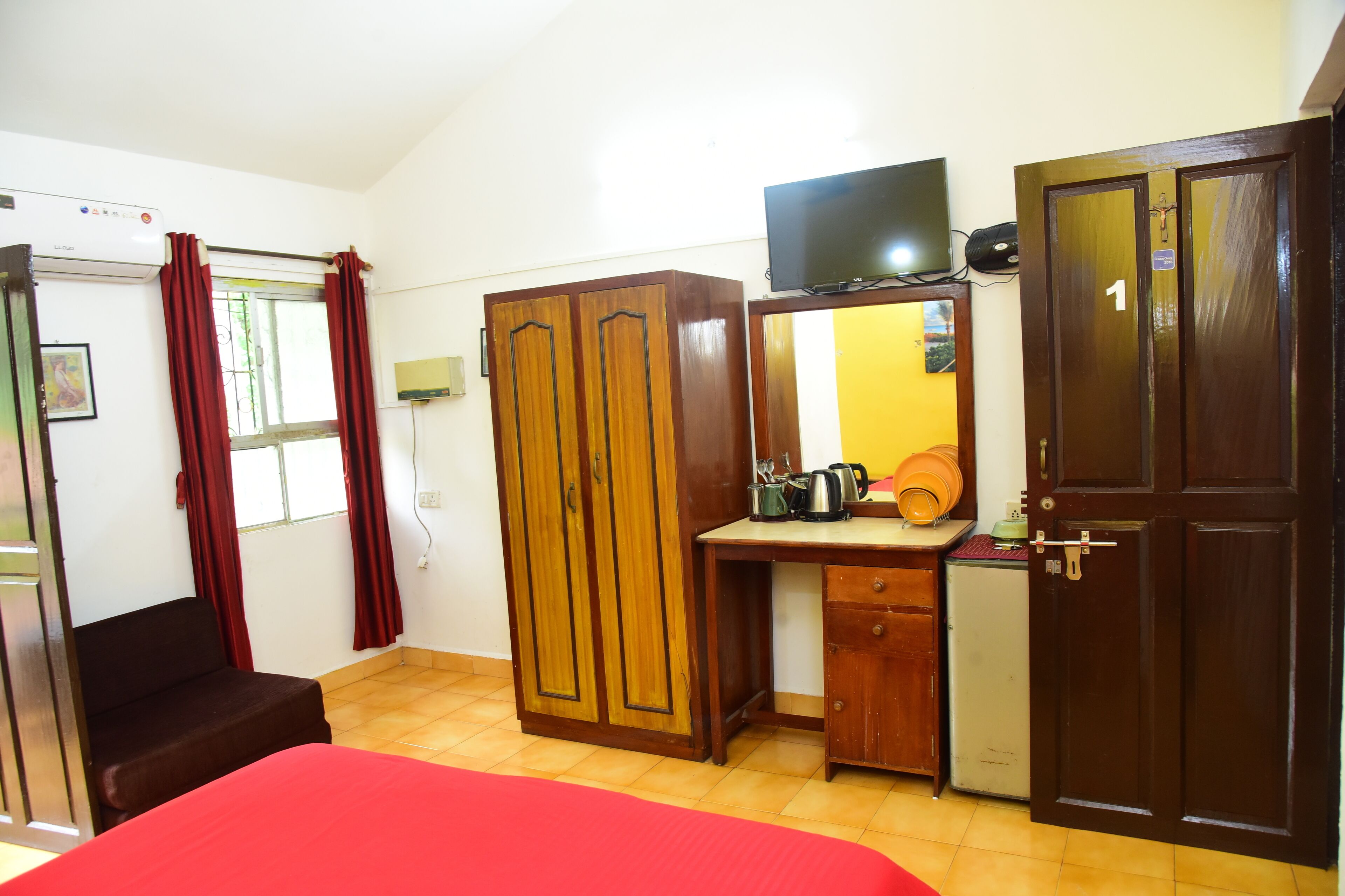 A room with a bed, a desk, a wardrobe, a television, and a small kitchenette.