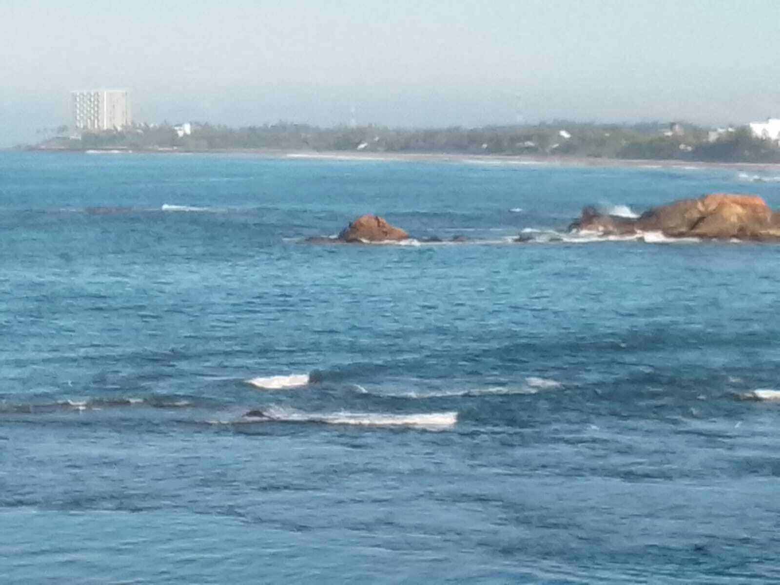 A coastal scene with clear blue water, rocky outcrops, and a distant building.