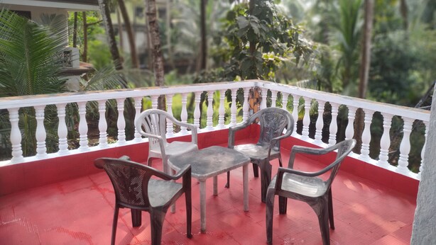 A balcony with a red floor, white balustrade, and several plastic chairs and a table. - JES Guest House (Majorda)
