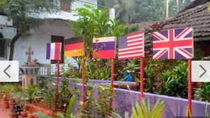 A garden with potted plants and a building with a cross. Flags of various countries are displayed. - JES Guest House (Majorda)