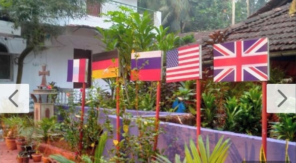 Un jardín con plantas en macetas y un edificio con una cruz. Se exhiben banderas de varios países.