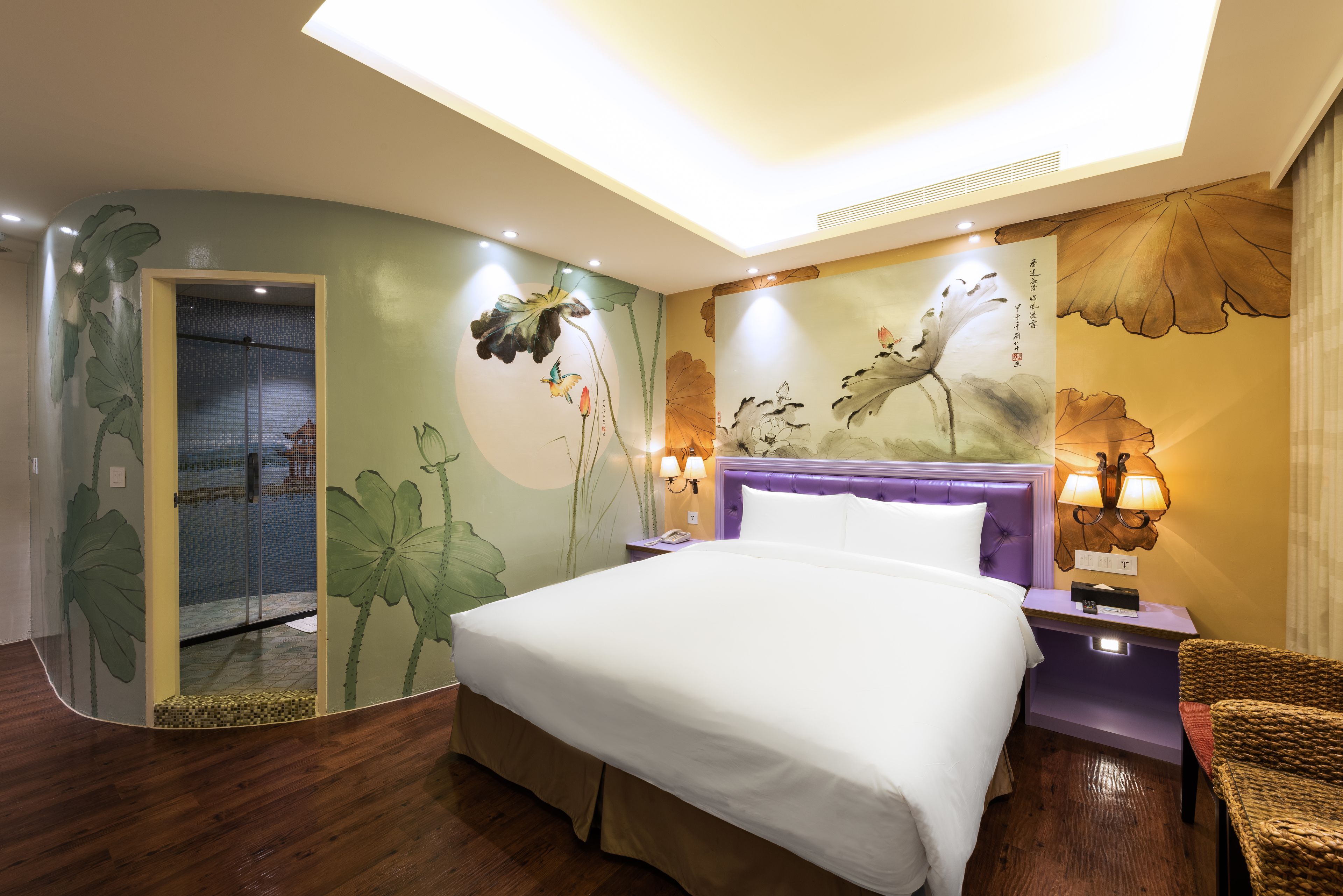A hotel room with a large bed, a shower area, and a wall with floral artwork.