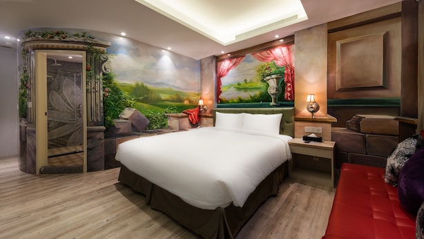 A bedroom with a large bed, a nightstand, a desk, and a seating area with a red sofa. - Shi Chi Hotel (Kaohsiung)