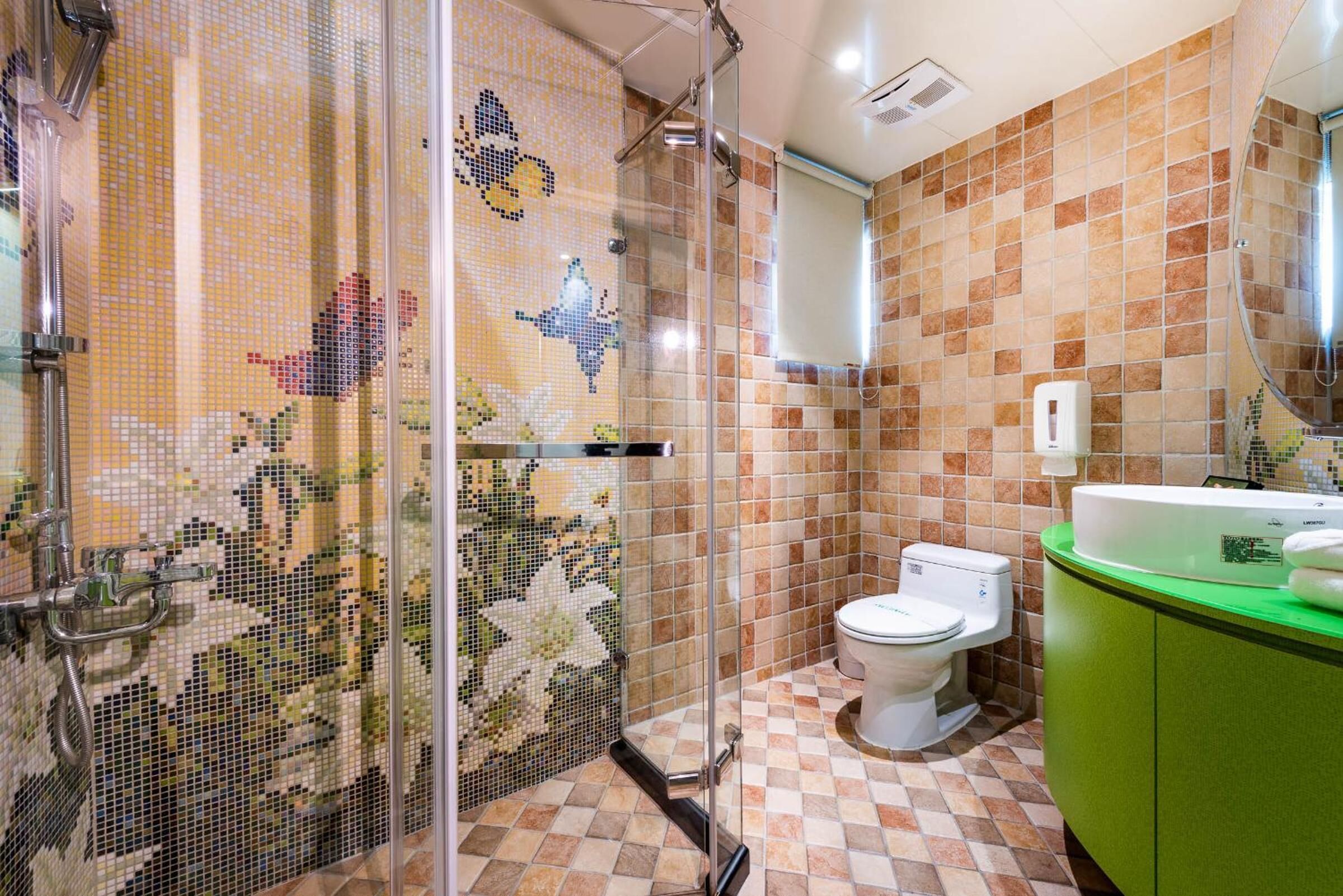 Casa de banho com azulejos de mosaico, cabine de duche, sanita e lavatório verde.