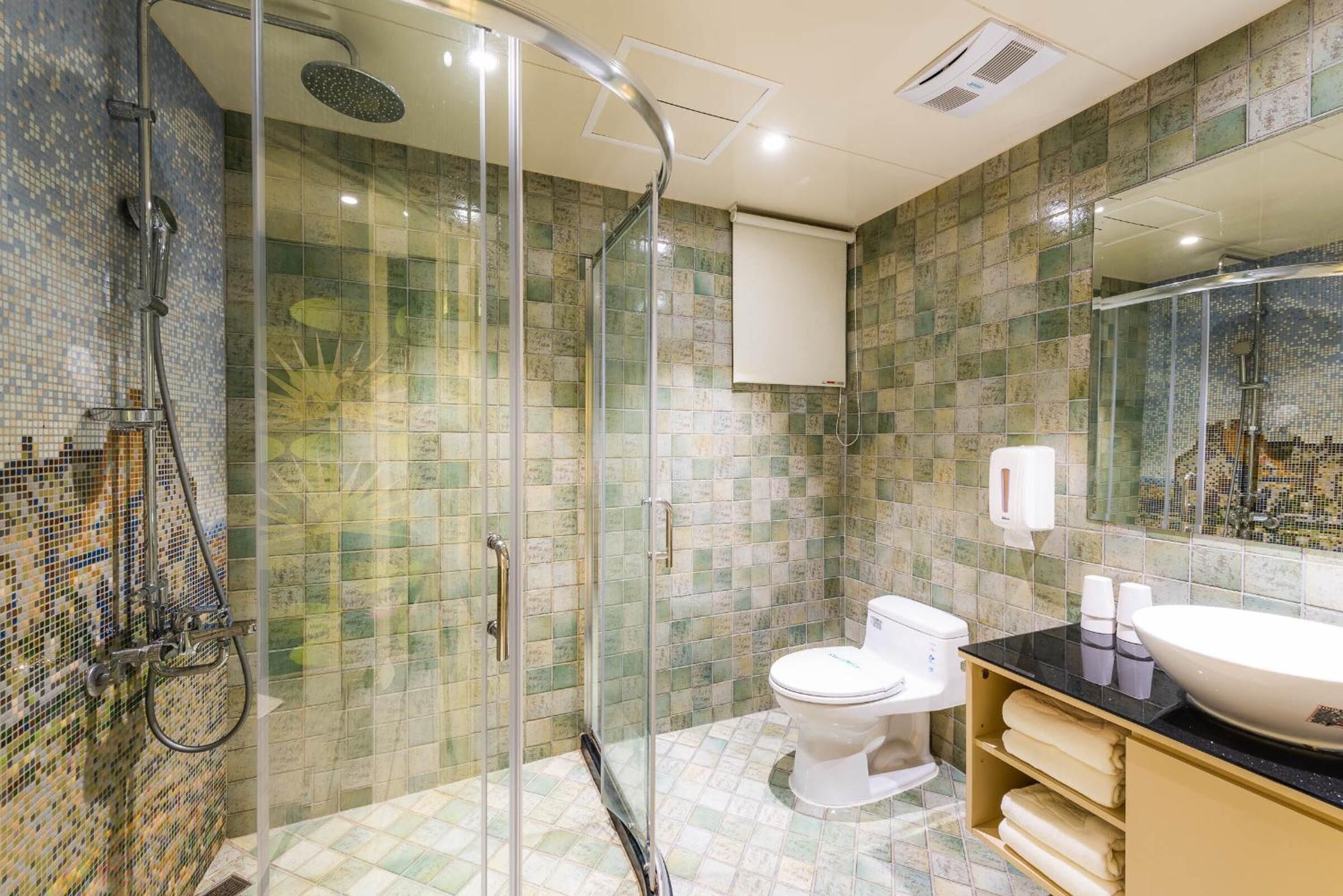 A bathroom with a glass-enclosed shower, a toilet, a sink with a black countertop, and a tiled wall with a mosaic pattern.