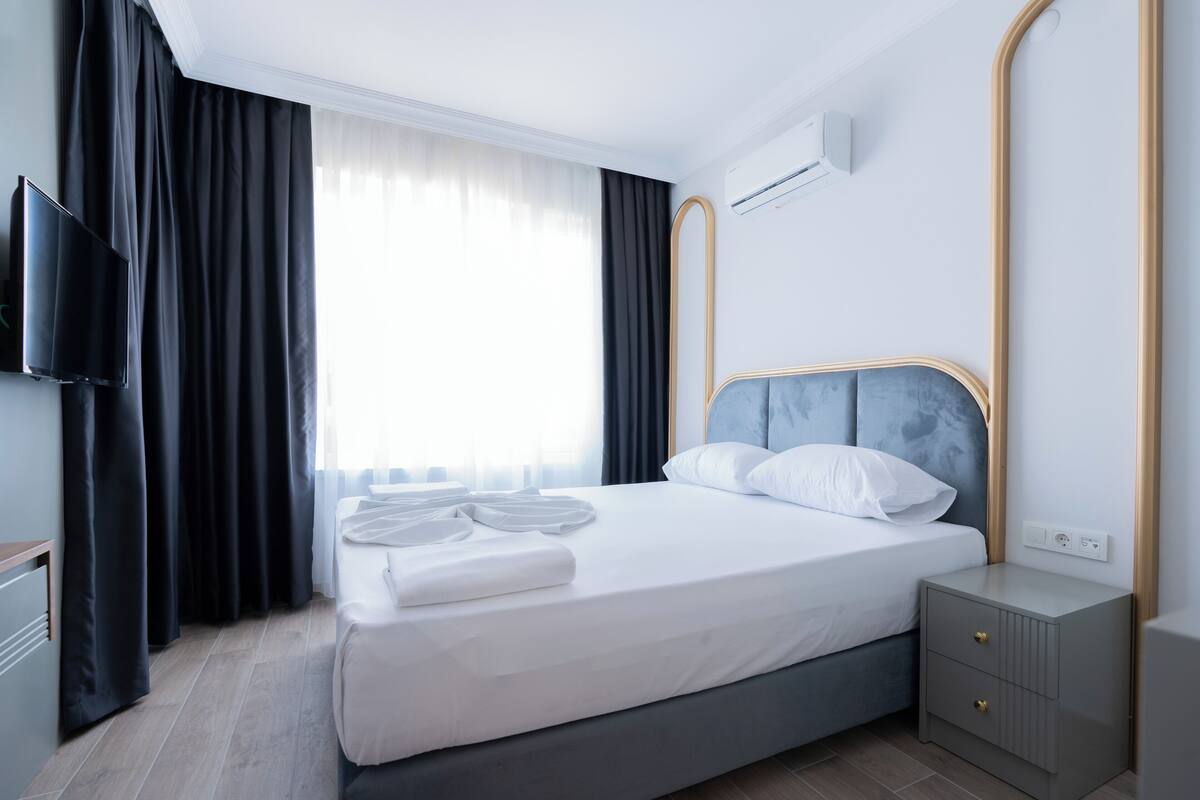 Une chambre d’hôtel moderne équipée d’un lit, d’une télévision, d’une table de chevet et d’une fenêtre avec des rideaux.