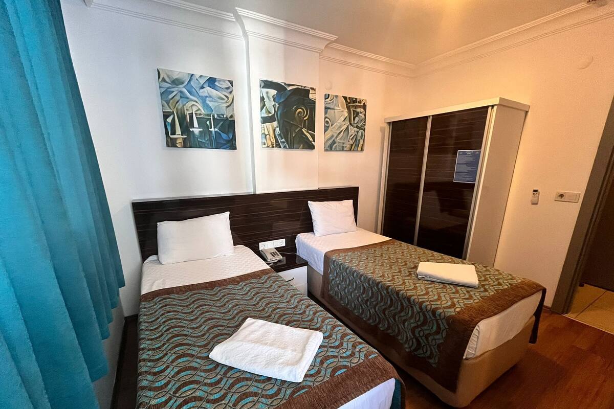 Une chambre d’hôtel avec deux lits simples, une armoire et des œuvres d’art abstraites accrochées au mur.