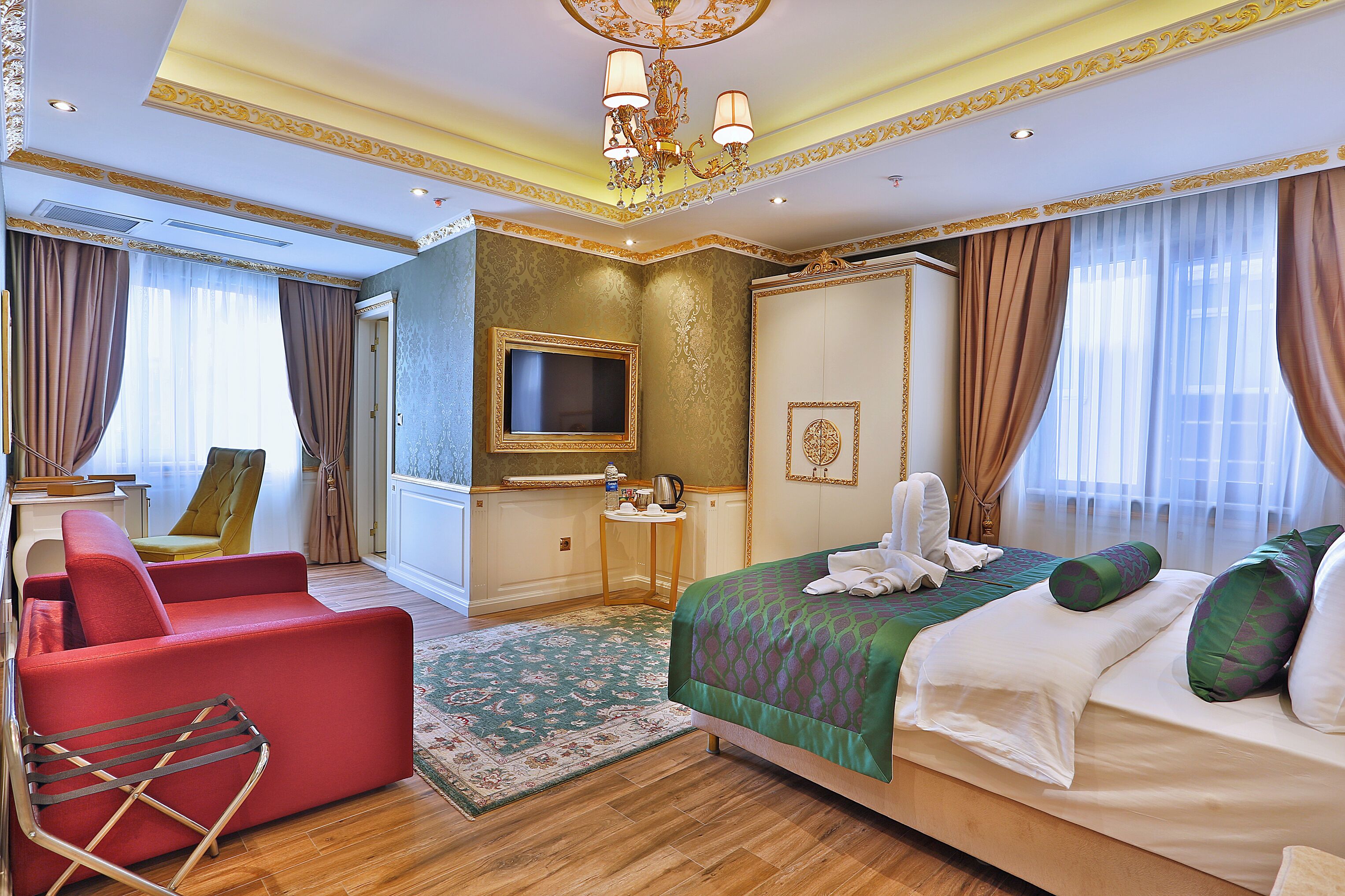 Habitación de hotel con una cama grande, un sillón rojo, un televisor y una mesita con un hervidor.