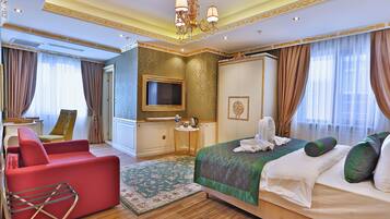 Habitación de hotel con una cama grande, un sillón rojo, un televisor y una mesita con un hervidor.