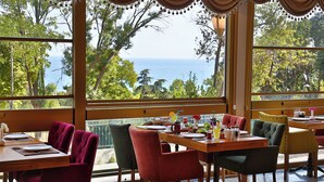 A dining area with a view of the sea, featuring a wooden table set with plates, glasses, and a fruit bowl. - Hotel Emirhan Palace (Istanbul)